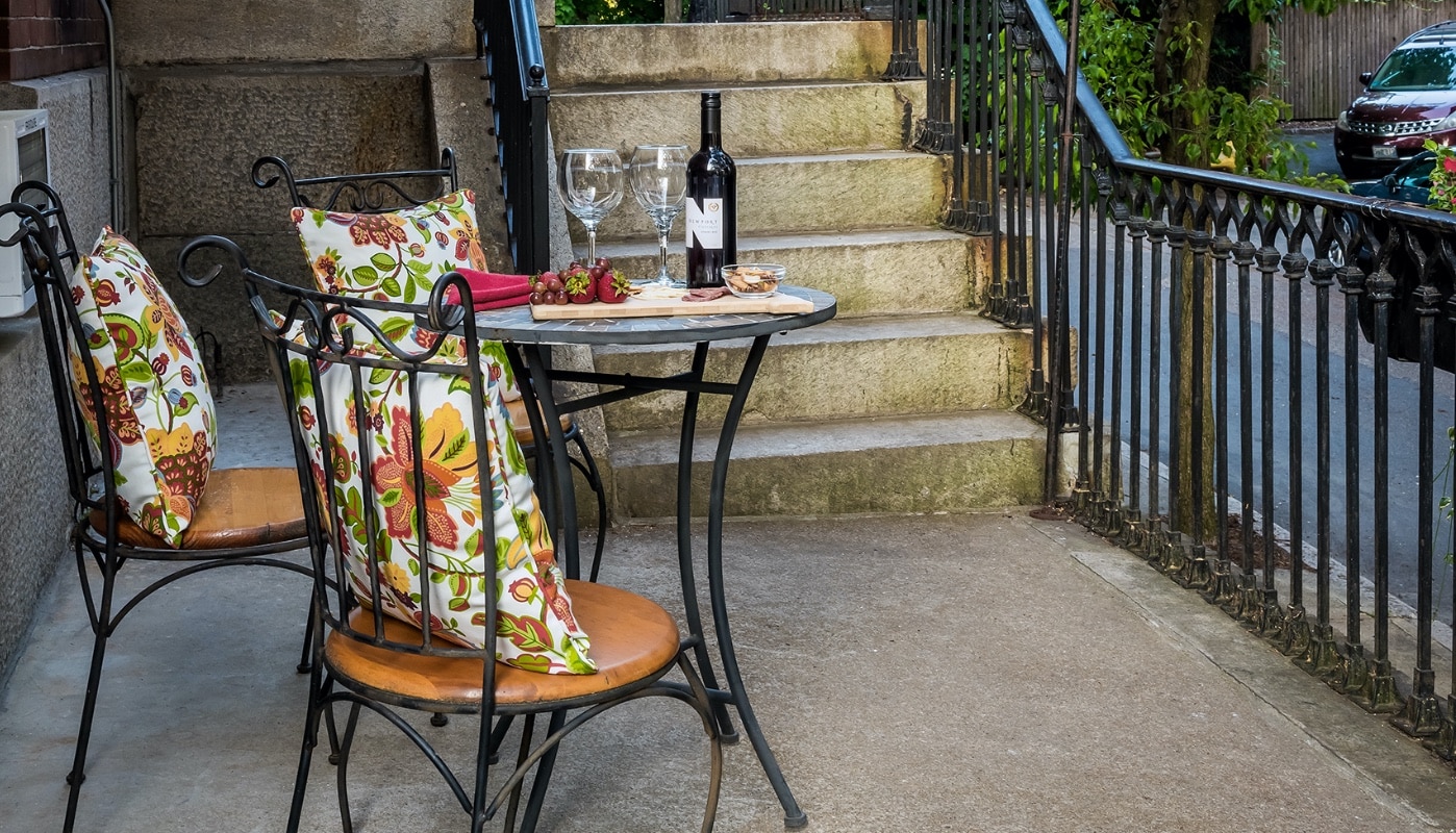Patio table featuring a charcuterie board, wine bottle and glasses with colorful throw pillow on the chairs.