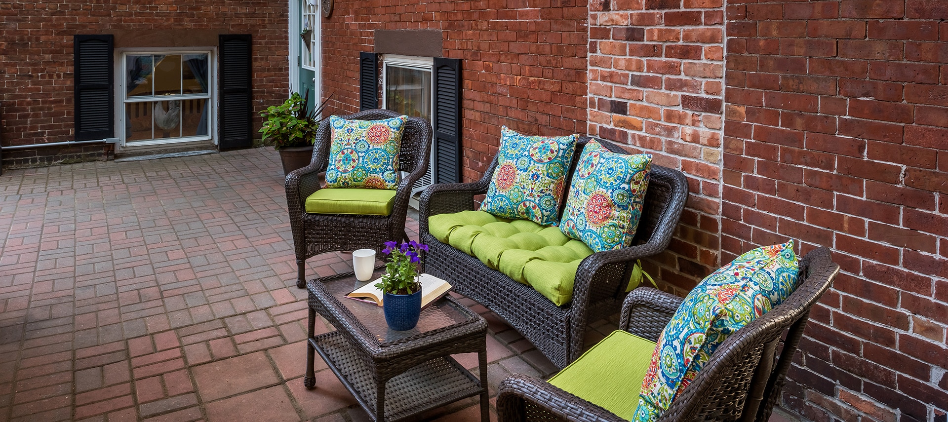 Brick patio featuring wicker furniture with bright green cushions and throw pillows.