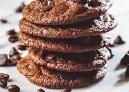 A stack of 5 chocolate espresso cookies with choclate morsels sprinkled around them.