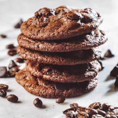 A stack of 5 chocolate espresso cookies with choclate morsels sprinkled around them.