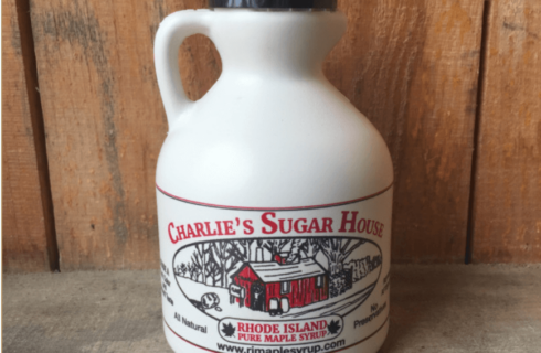 A beige pint sized bottle with a black cap featuring the logo of Charlie's Sugar House Maple Syrup.