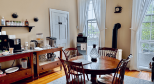 A room with a small round table witch four chairs and a table of refreshments.