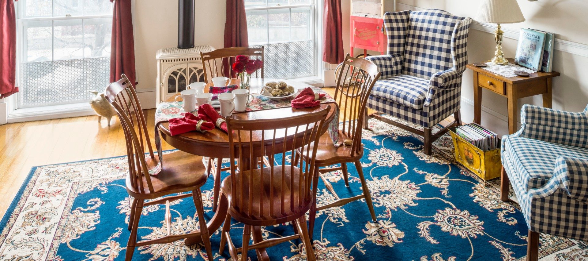 A large sitting room with a wooden table and chairs with refreshments and two checkered upholstered wingback chairs.