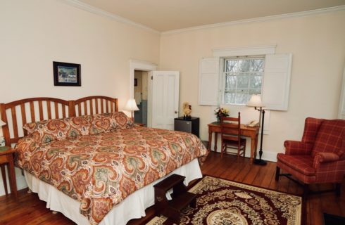 King bed with red patterned bedding, wooden desk, red wingback chair, and original hardwood floors.