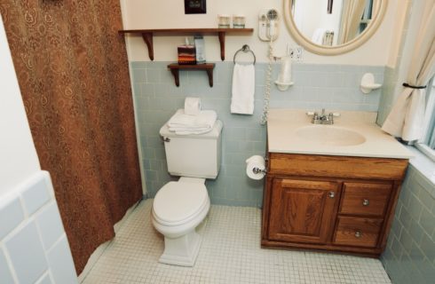 Bathroom in blue with a wooden vanity, toilet and gold patterned shower curtain.