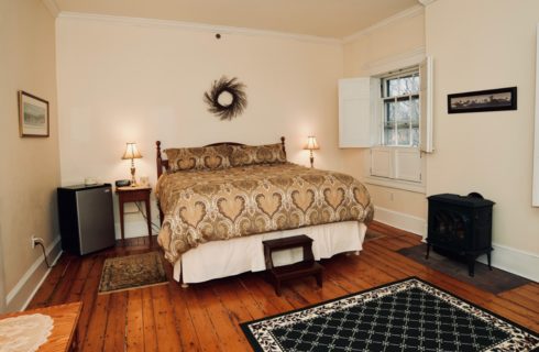 King bed in bedroom with windows with shutters and a patterned area rug over original hardwood floors.