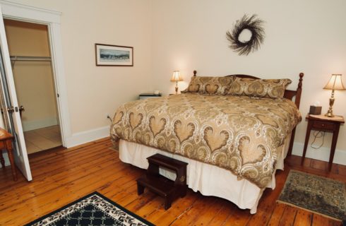 King bed in room with original hardwood floor and two tables with lamps.