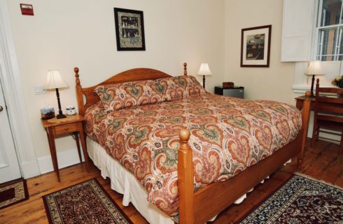Large four post bed in a bright patterned comforter with two nightstands holding lamps.