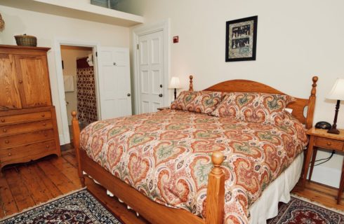 King bed in room with wide-plank wooden floor and wooden armoire.