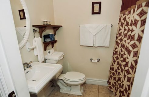 Bathroom with white pedestal vanity and stool with patterned shower curtain.