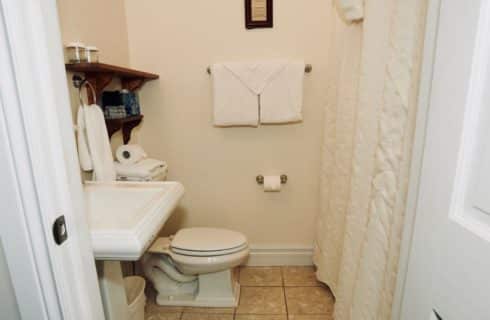 Bathroom with white pedestal sink, stool and white shower curtain.