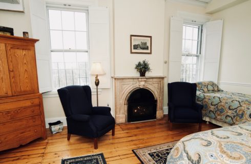 Spacious room with a fireplace, wooden armoire, two blue wingback chairs, and a king and twin bed.