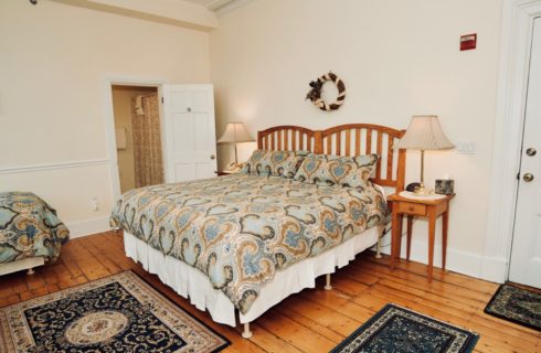 Large bright room with a wooden king bed and twin with blue patterned coverings, night stands with lamps, and original hardwood floors.