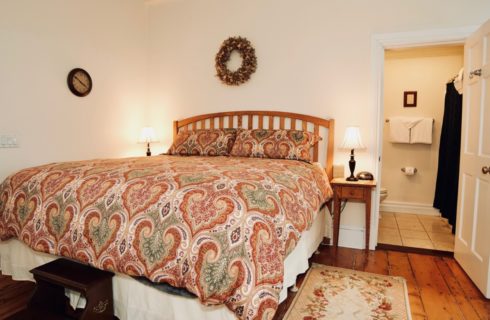 Large king sized bed made up with a bright patterned spread with two night tables and lamps in a room with cream walls.