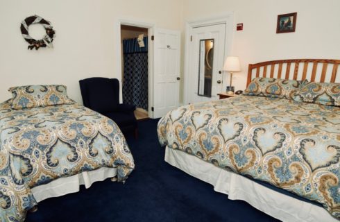 Bedroom featuring blue wall-to-wall carpeting with a king and twin bed made up in blue coverings with a blue wingback chair.
