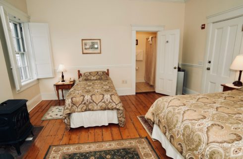 Large bright room with a king and a twin bed facing shuttered windows and a wood stove