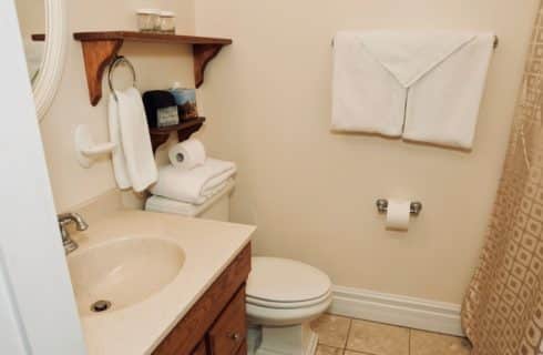 Bathroom painted white linen with a wooden vanity, a toilet, and a gold shower curtain.