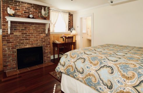 King bed with paisley blue comforter in a room with a brick fireplace and a wooden desk.