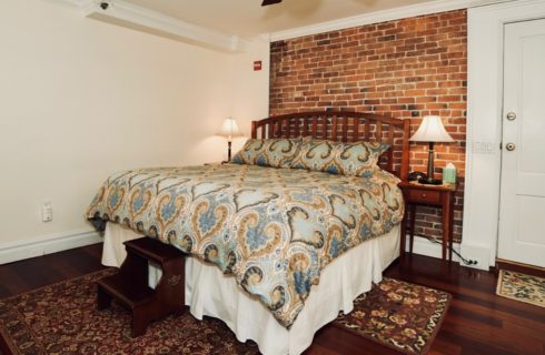 King bed with paisley blue comforter, two night stands with lamps, and a brick accent wall.