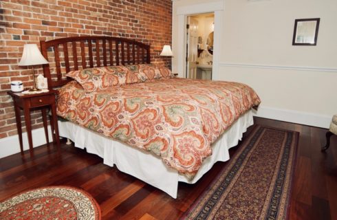 King bed made up in a paisley bedspread with two end tables with lamps in a room with hardwood floors.