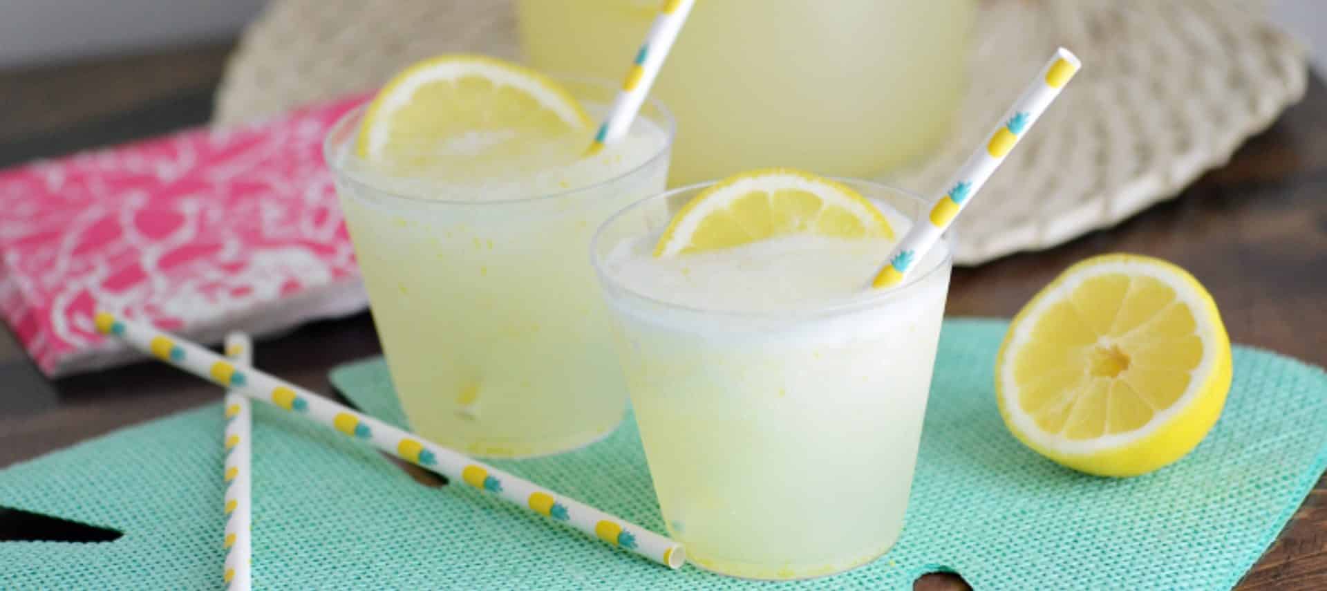 Two small clear plastic cups filled with frozen lemonade and a slice of lemon with a straw.