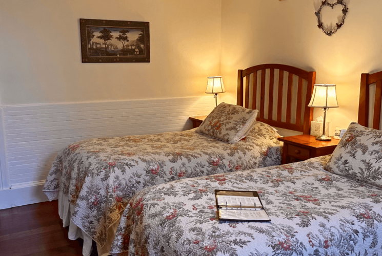 A room with two beds and bed side tables with lamps.