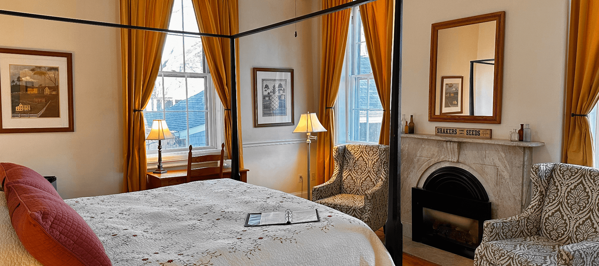 A four-poster bed facing a marble fireplace and 2 chairs.