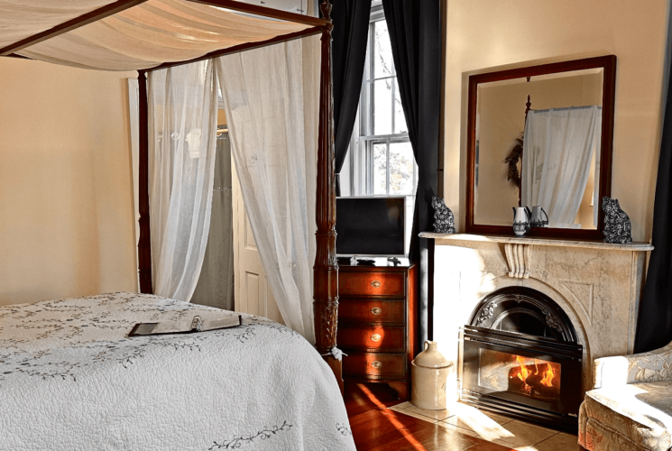 A room with a canopy bed, marble fireplace, and a chair.