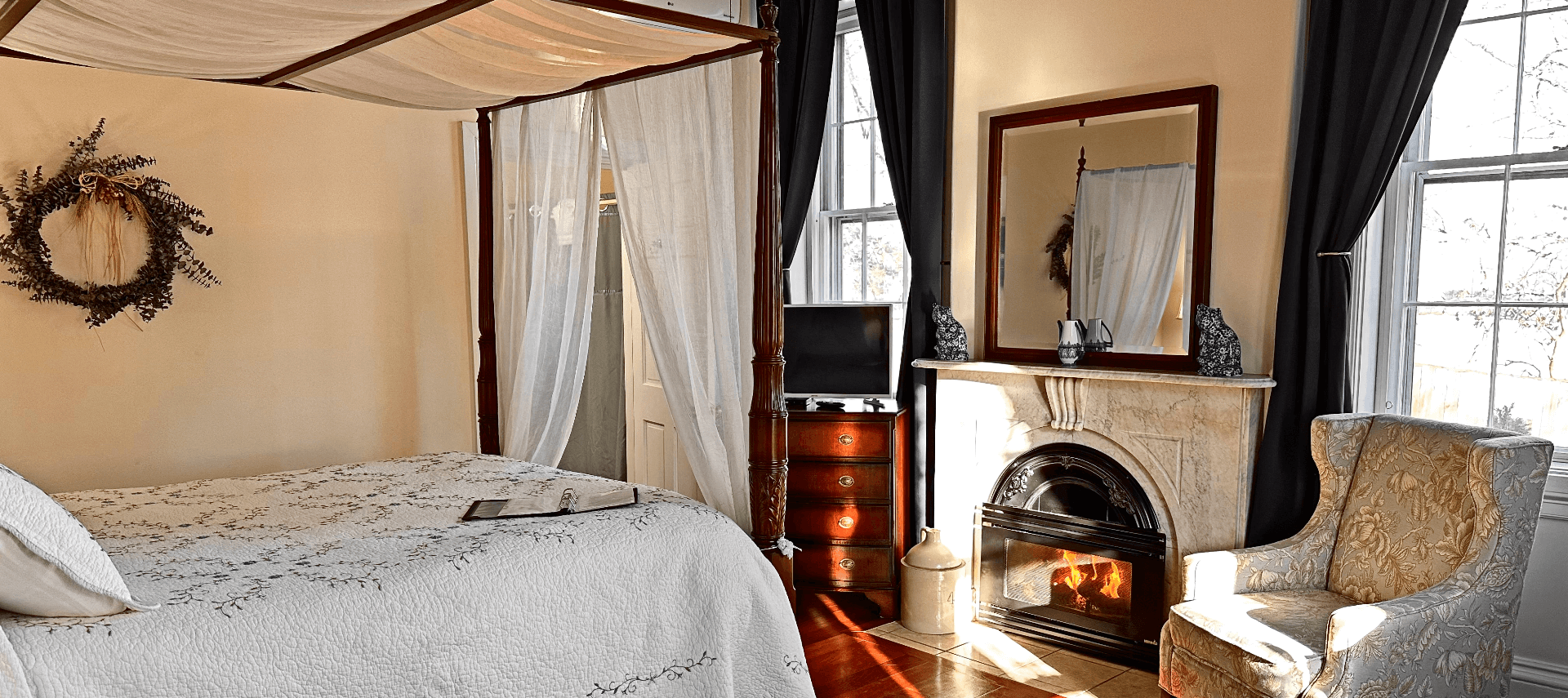 A room with a canopy bed, marble fireplace, and a chair.