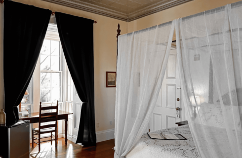 A room with a canopy bed, and a desk with chair in an alcove.