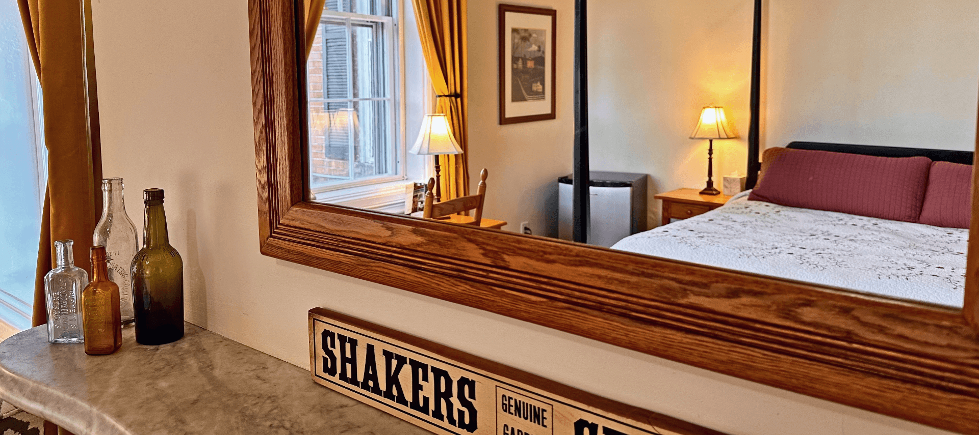 A marble mantel with vintage glass bottles and a mirror reflecting a room.