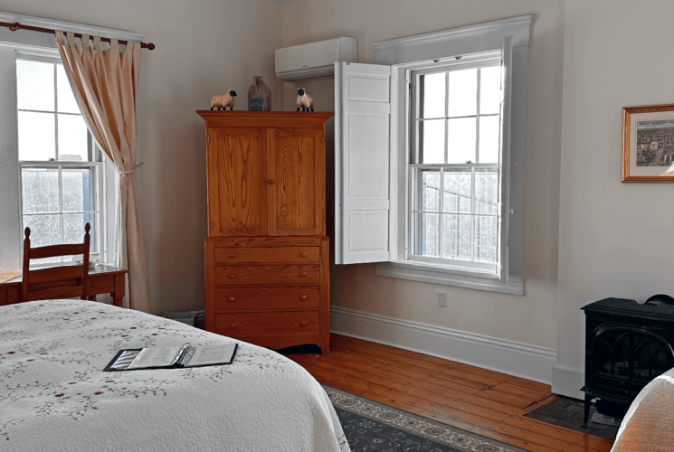 A room with 2 beds, a wood stove, armoire, and desk with a chair.