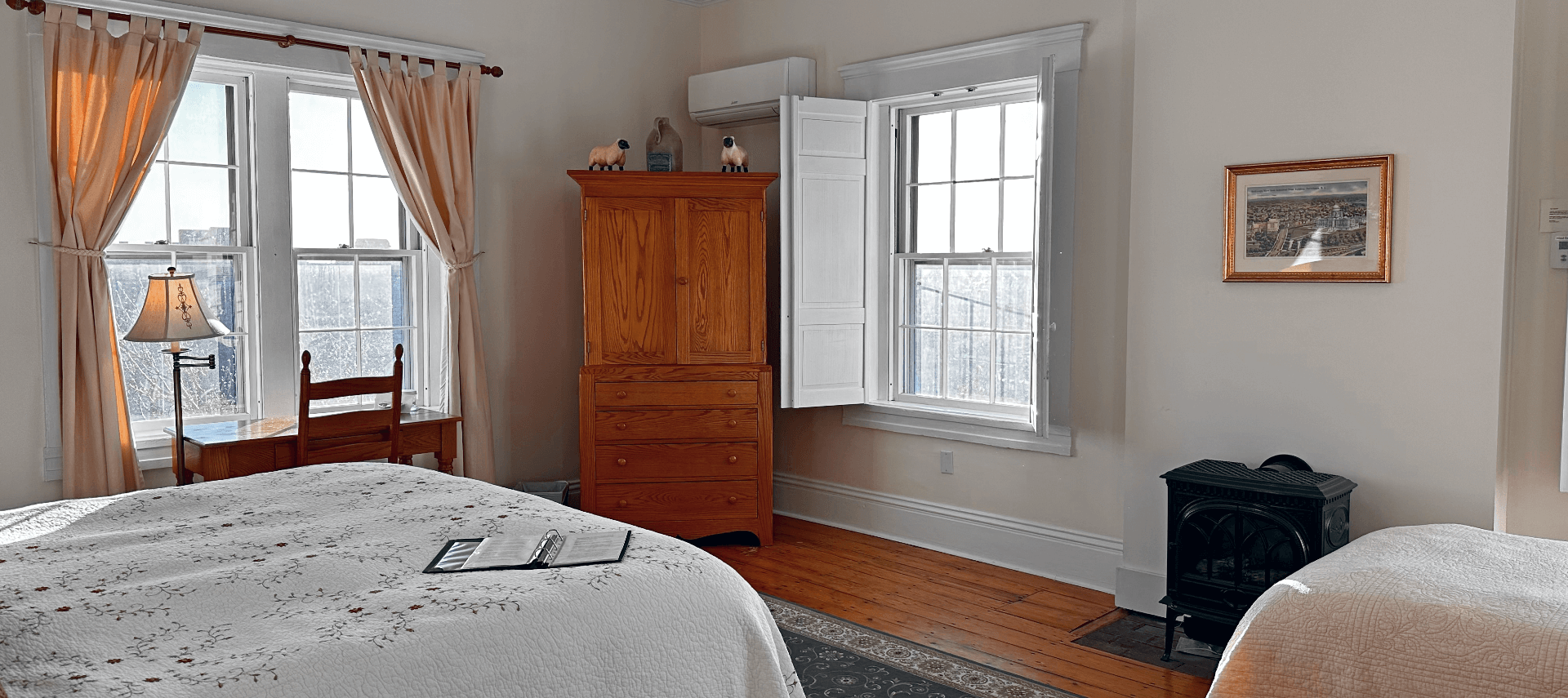 A room with 2 beds, a wood stove, armoire, and desk with a chair.
