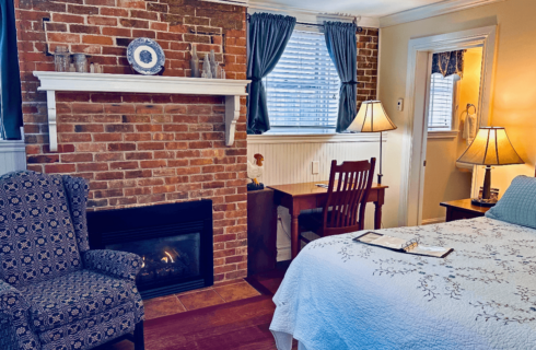 A room with a bed, brick fireplace, a chair, and a desk with chair.