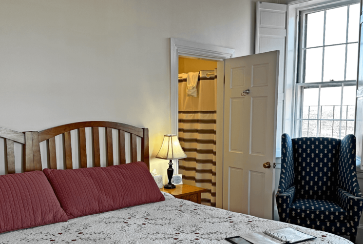 A room with a bed, a chair, and a wood stove.