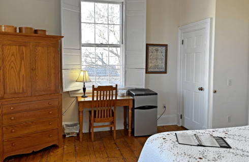 A room with a bed, armoire, desk with chair, and a mini fridge.