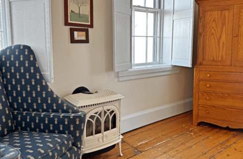 A room with a chair, wood stove, and an armoire.