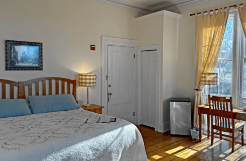 A room with a bed, mini fridge, and desk with a chair.