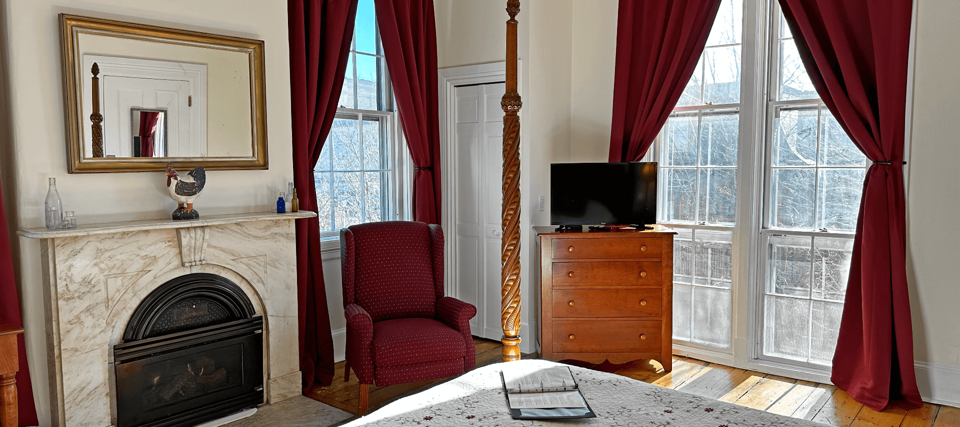 A room with a 4 poster bed, marble fireplace, and a chair.