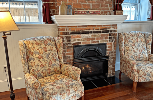 A room with a brick fireplace, 2 chairs, and a floor lamp.