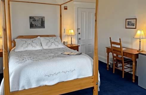 A room with a four-poster bed and a desk with chair.