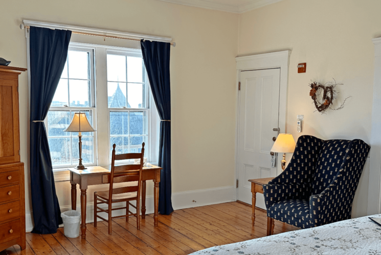 A room with a bed, armoire, desk with chair, and a chair.