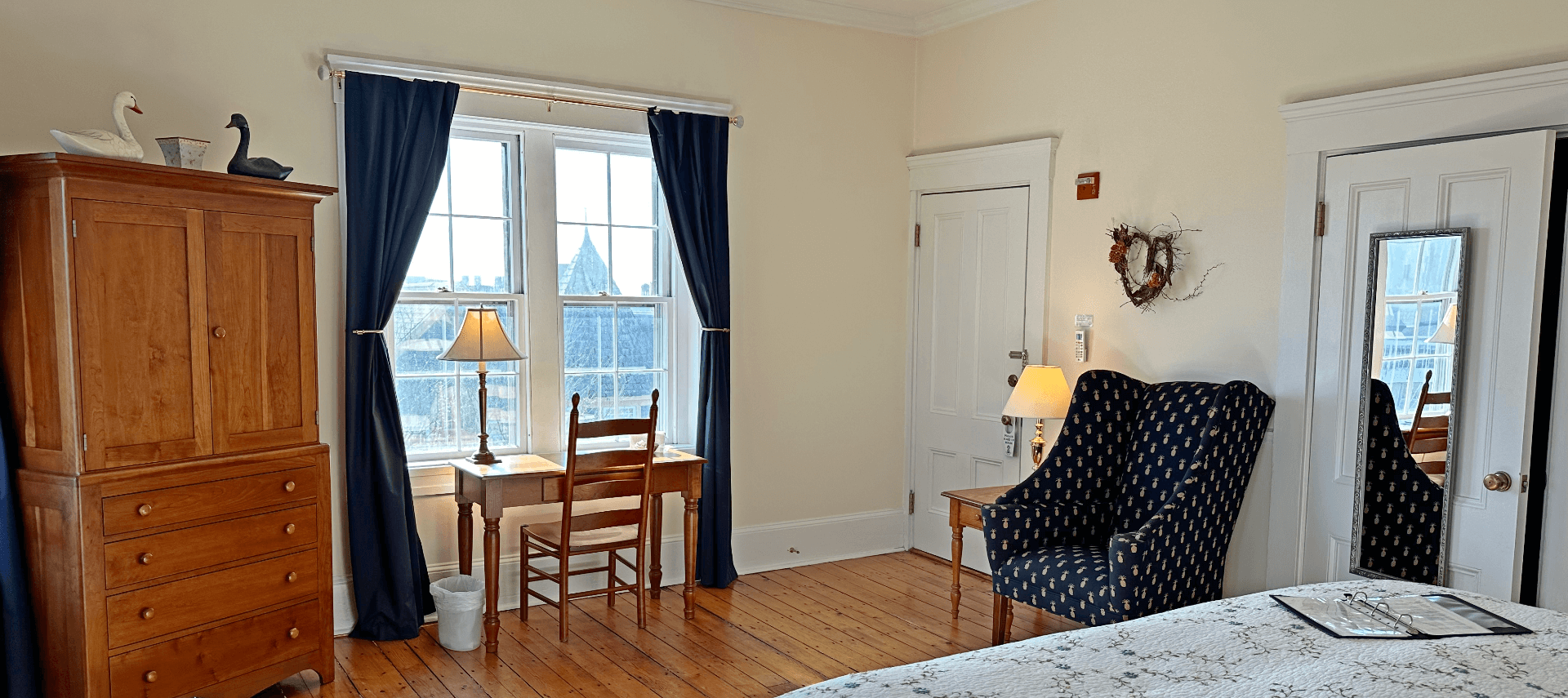 A room with a bed, armoire, desk with chair, and a chair.