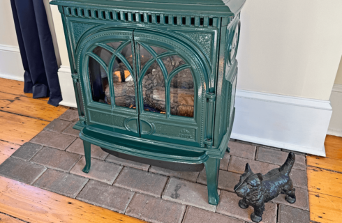 A wood stove on a brick hearth with a scotty dog figurine.