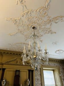 A large glass candle light chandelier hanging from a beautiful plaster ceiling.