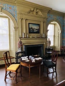 A reading room with a round mahogany table in front of a grand fireplace.