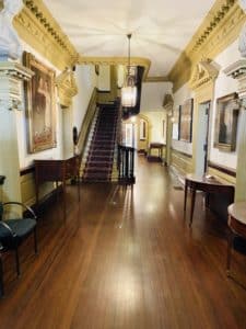 A long hallway featuring hardwood floors leading to a grand mahogany staircase.