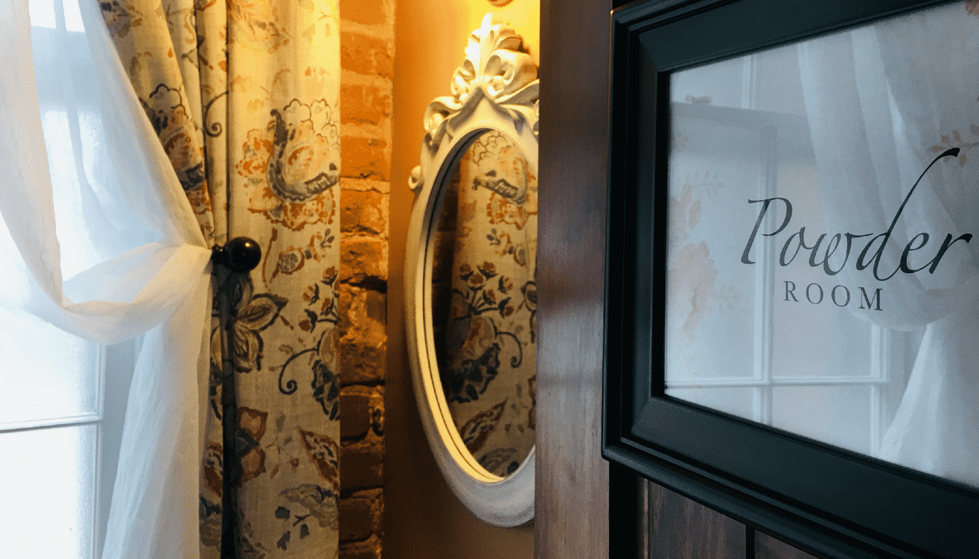 Open door showing a mirror and curtains with a "powder room" sign .