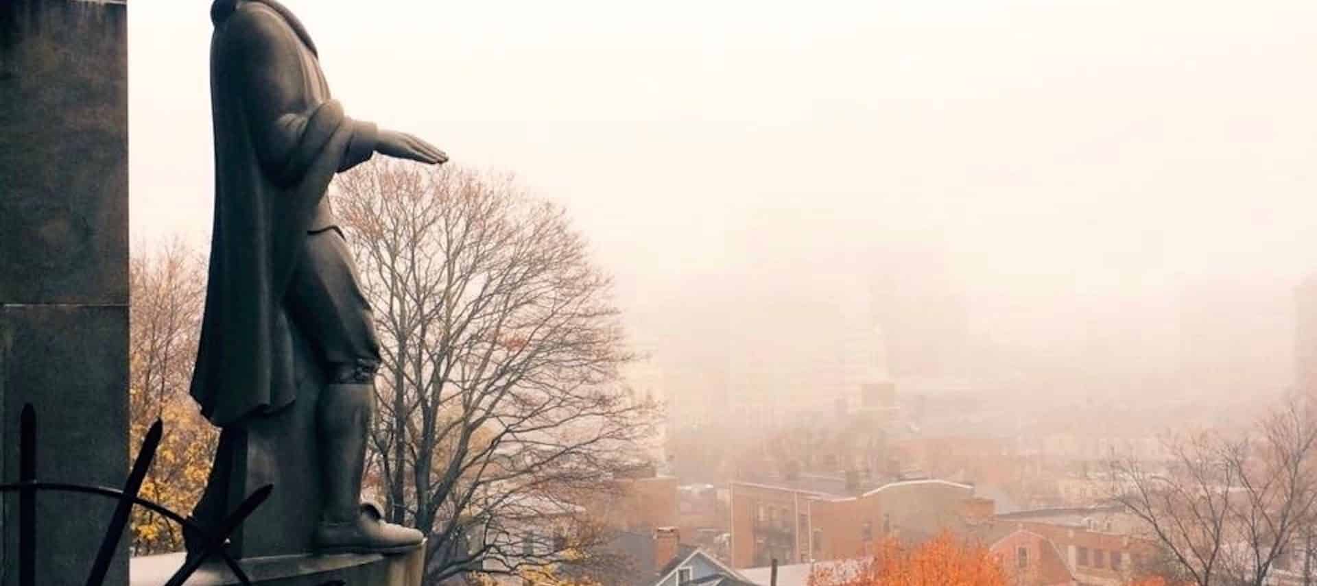 A large statue of Roger Williams situated on a hill overlooking Providence on a foggy fall day.