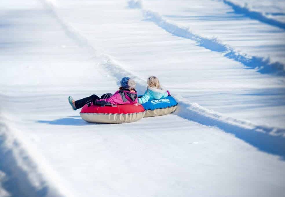 Two young girls sitting in snowtubes gliding down a snowy hillside.